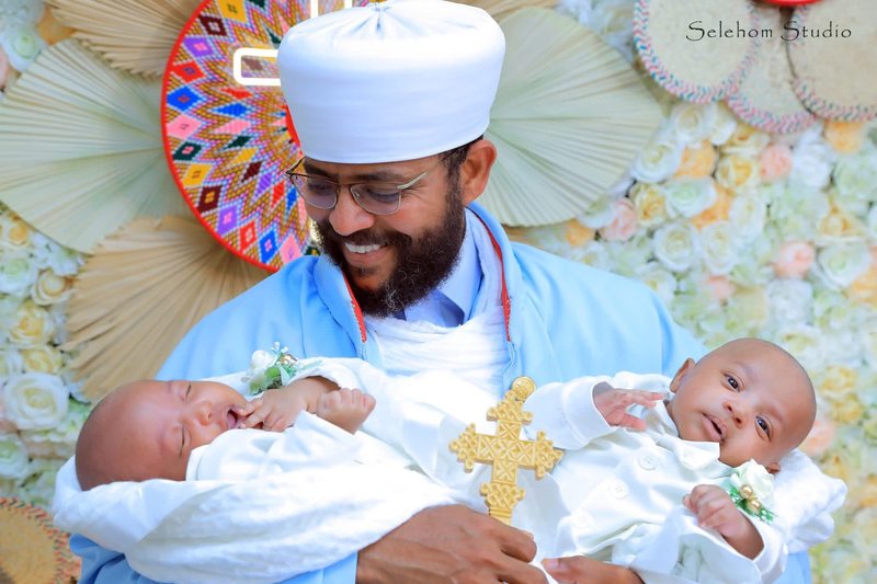 Man in blue ceremonial robes holding two infants