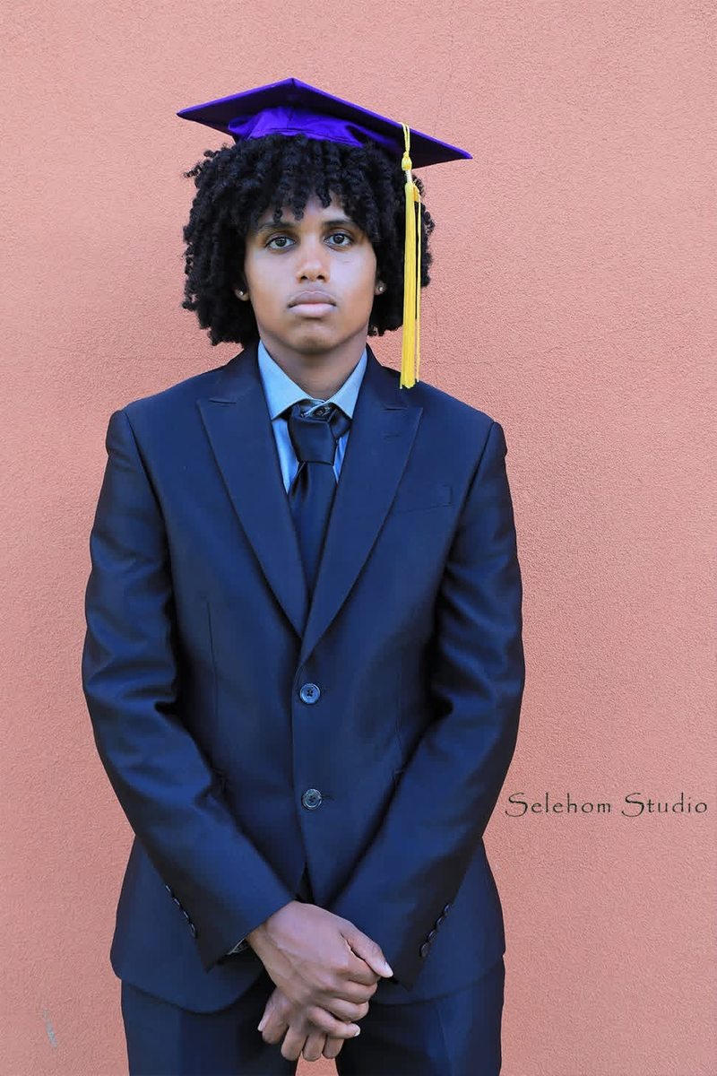 Graduate in a purple cap and navy suit against a warm-colored wall