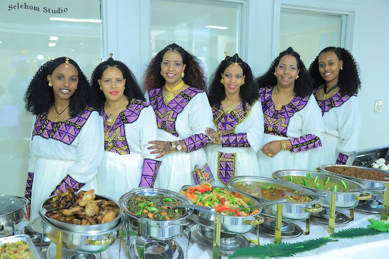 Women in traditional dress gathered behind a table of prepared food