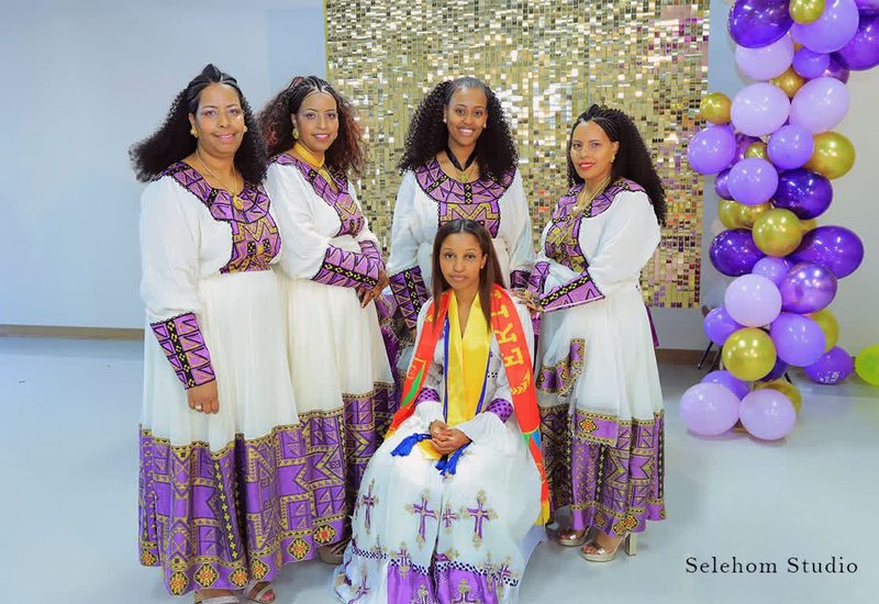Women in matching purple and white dresses posing beside balloons