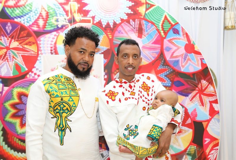 Two men standing with an infant against a colorful backdrop